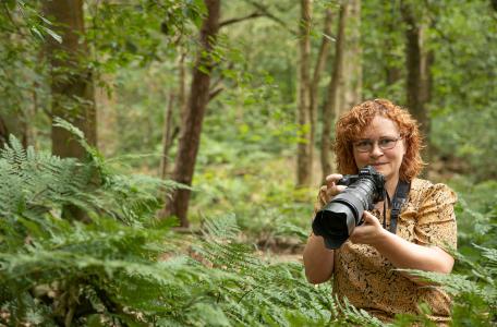 Mignon van den Wittenboer terwijl ze met haar fotocamera opnamen aan het maken is in een varenrijk loofbos.
